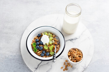 Homemade granola with greek yogurt and fruits in a bowl on marble serving board. Healthy breakfast food, oat cereals