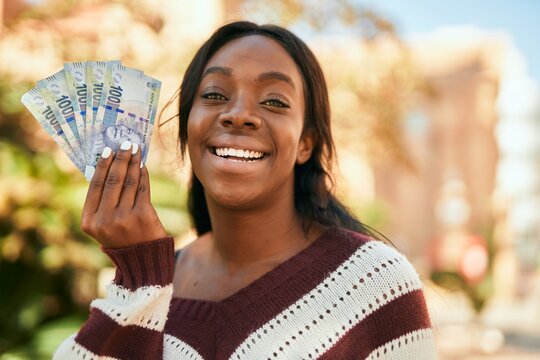 Young african american woman smiling happy holding south africa rands at the park.