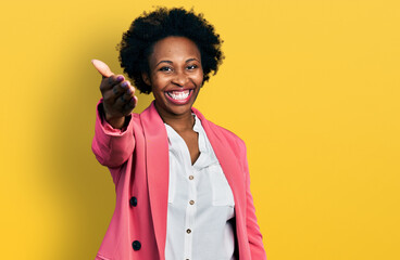 Obraz na płótnie Canvas African american woman with afro hair wearing business jacket smiling friendly offering handshake as greeting and welcoming. successful business.