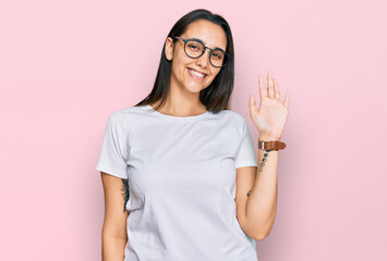 Young hispanic woman wearing casual white t shirt waiving saying hello happy and smiling, friendly welcome gesture