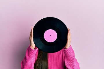 Woman holding retro vinyl disc covering face over pink background