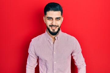 Handsome man with beard wearing casual red shirt looking positive and happy standing and smiling with a confident smile showing teeth