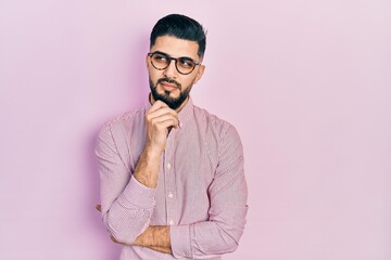 Handsome man with beard wearing casual shirt and glasses serious face thinking about question with...