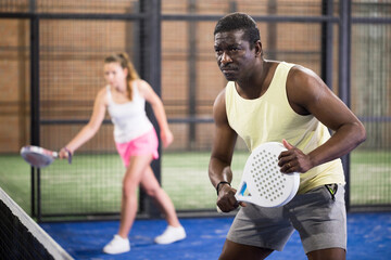 Fototapeta premium Sporty afro american man in yellow t-shirt playing padel tennis indoor