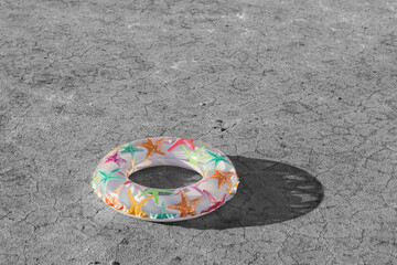colorful inflatable ring for swimming, lies on dry monochrome ground with cracks, concept