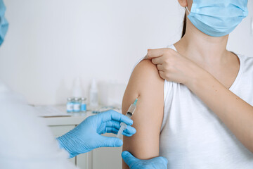 Hand of medical staff in blue gloves injecting covid-19 vaccine to arm muscle of human for...