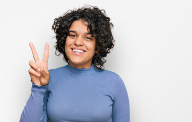 Young hispanic woman with curly hair wearing casual clothes showing and pointing up with fingers number two while smiling confident and happy.