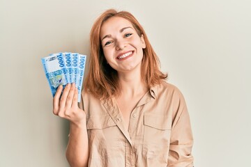 Young caucasian woman holding hungarian forint banknotes looking positive and happy standing and smiling with a confident smile showing teeth