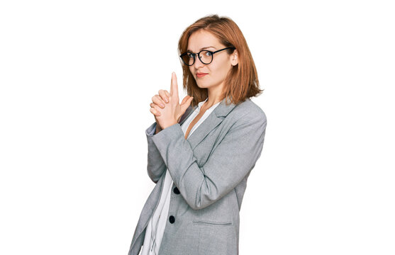 Young caucasian woman wearing business style and glasses holding symbolic gun with hand gesture, playing killing shooting weapons, angry face