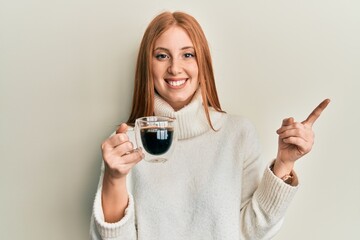 Young irish woman drinking a cup of coffee smiling happy pointing with hand and finger to the side