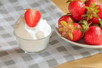 Ripe strawberries in a white plate and cream on the table
