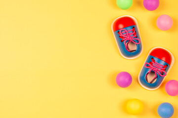 Wooden educational toy shoes and colorful balls on pastel yellow background. Top view
