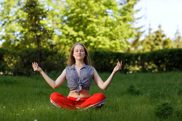 Young woman practicing yoga in the park and relax in nature. Shallow focus.