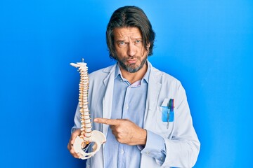 Fototapeta premium Middle age handsome traumatologist man holding anatomical model of spinal column depressed and worry for distress, crying angry and afraid. sad expression.