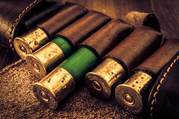 Hunting ammunition 12 gauge in leather bandolier on a wooden table. Focus on the cartridges