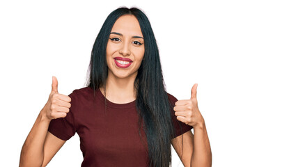 Young hispanic girl wearing casual t shirt success sign doing positive gesture with hand, thumbs up smiling and happy. cheerful expression and winner gesture.