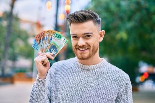 Young caucasian man smiling happy holding australian dollars at the park.
