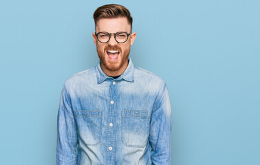 Young redhead man wearing casual denim shirt sticking tongue out happy with funny expression. emotion concept.