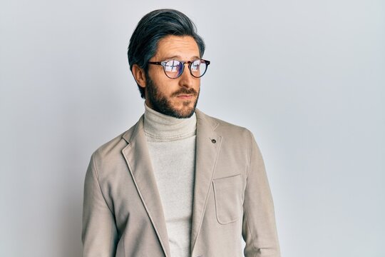 Young hispanic man wearing business jacket and glasses smiling looking to the side and staring away thinking.