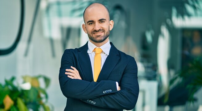 Young hispanic bald businessman with arms crossed smiling happy at the city.