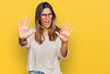 Young woman wearing casual clothes and glasses afraid and terrified with fear expression stop gesture with hands, shouting in shock. panic concept.