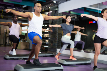 Fototapeta na wymiar Athletic people performing step aerobics in fitness club
