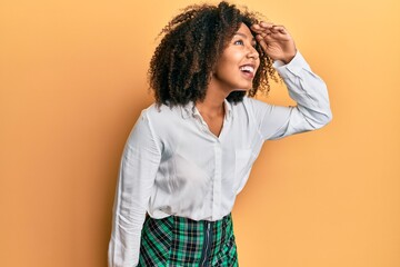 Beautiful african american woman with afro hair wearing scholar skirt very happy and smiling looking far away with hand over head. searching concept.