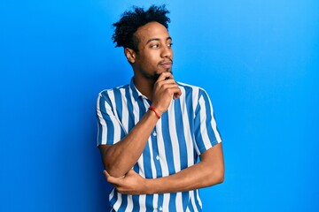 Young african american man with beard wearing casual striped shirt with hand on chin thinking about question, pensive expression. smiling with thoughtful face. doubt concept.