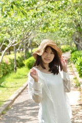 新緑の公園でポーズをとる麦わら帽子を被った若い笑顔の女性