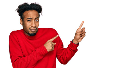 Young african american man with beard wearing casual winter sweater pointing aside worried and nervous with both hands, concerned and surprised expression