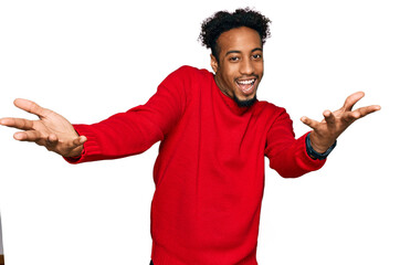 Young african american man with beard wearing casual winter sweater smiling cheerful offering hands giving assistance and acceptance.