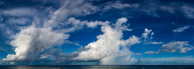 Colorful seascape with a rainbow on the sky, clouds reflected in the water, natural background panoramic view banner