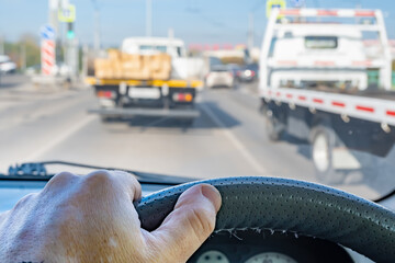 the driver's hand on the steering wheel inside the car during a traffic jam in the city traffic flow against the background of two trucks in front of a pedestrian crossing and a traffic light