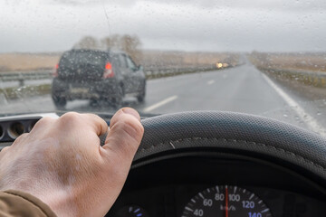 driver hand on the steering wheel inside the car and raindrops on the windshield