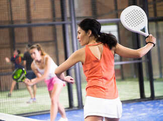 Woman playing padel in a green grass padel court indoor behind the net