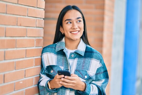Young latin girl smiling happy using smartphone at the city.