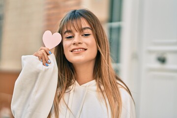 Caucasian sporty teenager girl smiling happy holding heart at the city.