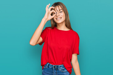 Teenager caucasian girl wearing casual red t shirt doing ok gesture with hand smiling, eye looking through fingers with happy face.