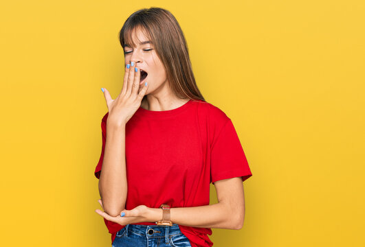 Teenager caucasian girl wearing casual red t shirt bored yawning tired covering mouth with hand. restless and sleepiness.
