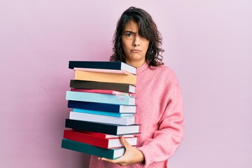 Young hispanic woman holding a pile of books skeptic and nervous, frowning upset because of problem. negative person.