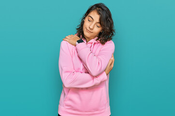 Young hispanic woman wearing casual sweatshirt hugging oneself happy and positive, smiling...