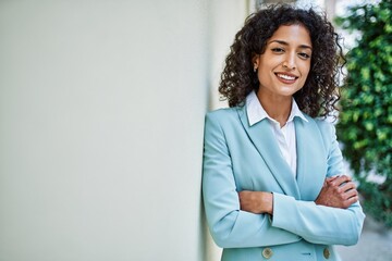 Young hispanic business woman wearing professional look smiling confident at the city leaning on the wall