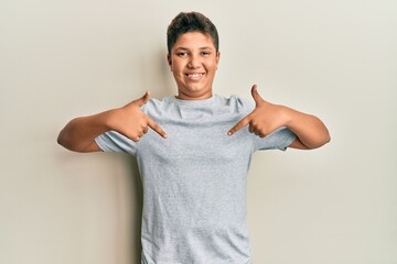 Teenager hispanic boy wearing casual grey t shirt looking confident with smile on face, pointing...