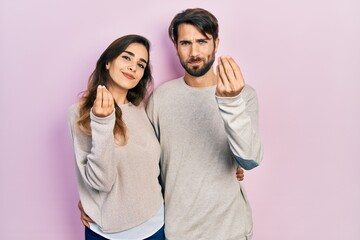Naklejka premium Young hispanic couple wearing casual clothes doing money gesture with hands, asking for salary payment, millionaire business