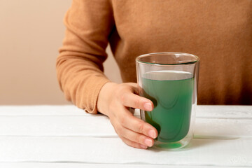 Woman hand holding cup of chlorophyll water on white table