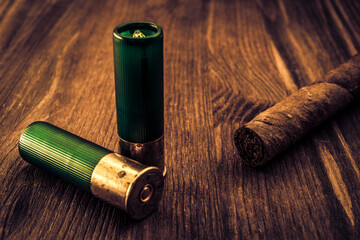 Two 12 gauge bullets and cuban cigar lying on a wooden table. Focus on the cuban cigar