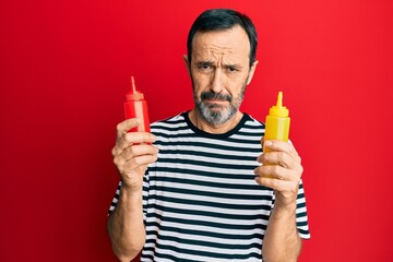 Middle age hispanic man holding ketchup and mustard bottle depressed and worry for distress, crying angry and afraid. sad expression. - Powered by Adobe