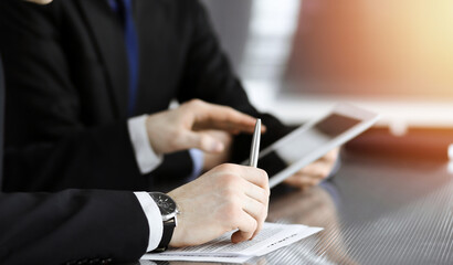 Businessman using tablet computer and work together with his colleague in sunny modern office, close-up. Unknown business people at meeting. Teamwork and partnership concept