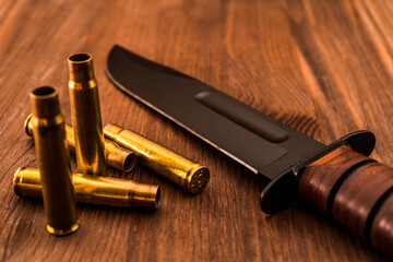 Empty shells from the rifle and combat knife lying on a wooden table. Focus on the shells