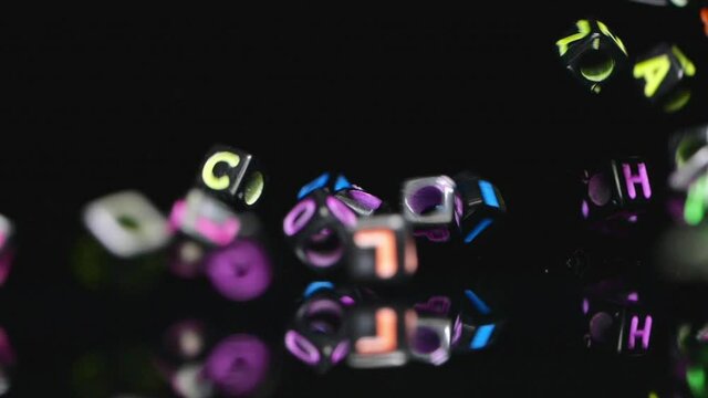 Multi-colored letter beads fall on to mirror in slow motion.